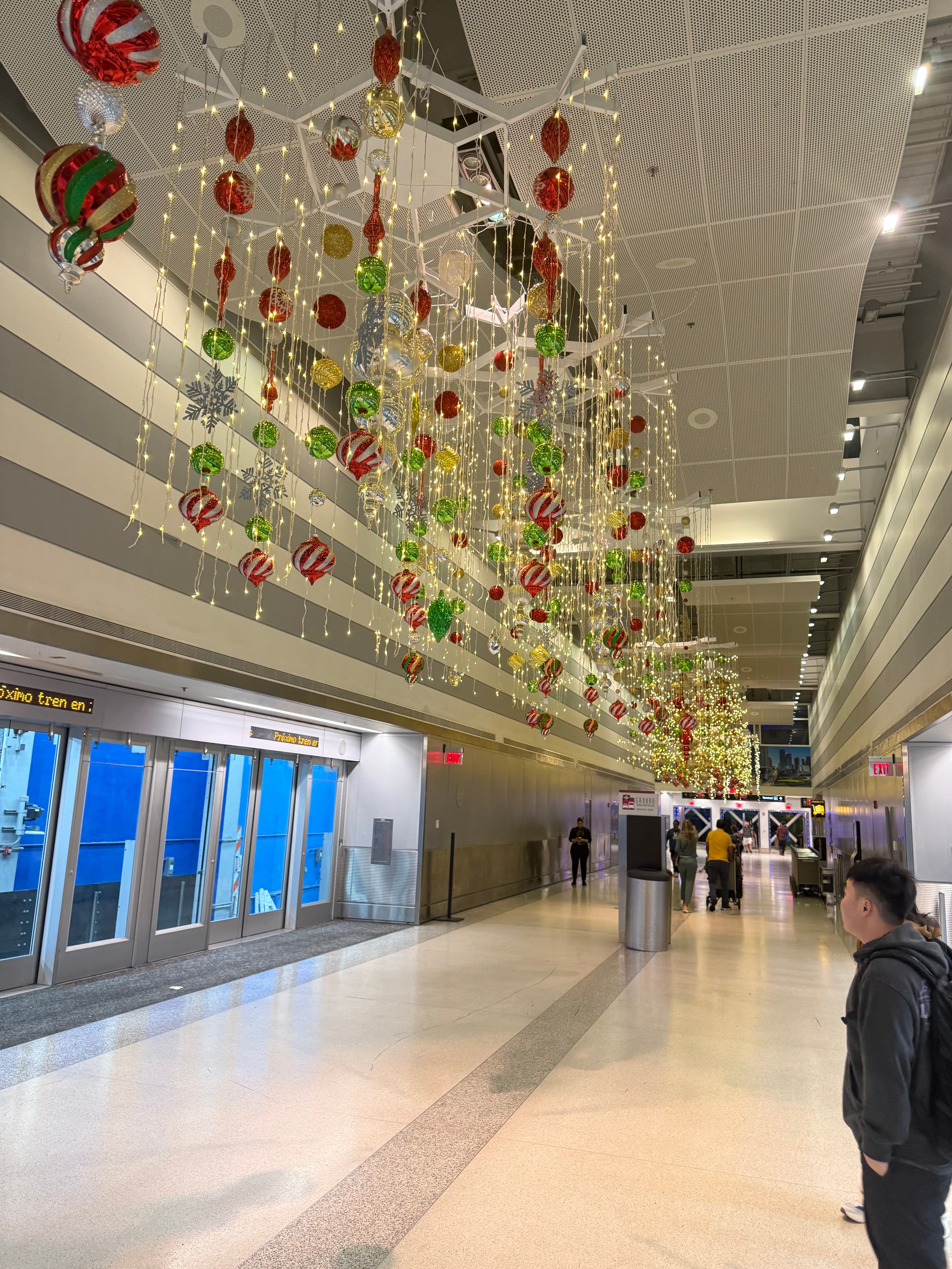 Red and green ornaments and lights hang from the ceiling of a modern transit station.