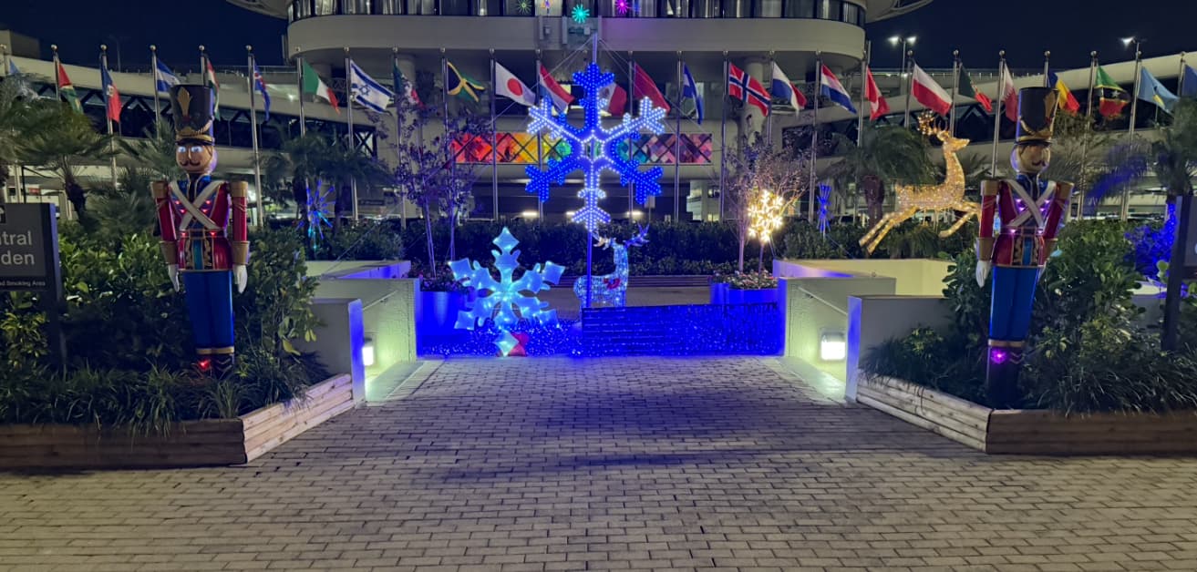 Nutcracker statues and glowing blue snowflakes decorate a walkway lined with international flags at night.
