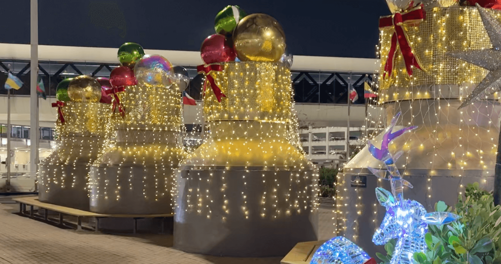 Light-wrapped structures topped with giant colorful ornaments and a glowing blue reindeer at night.